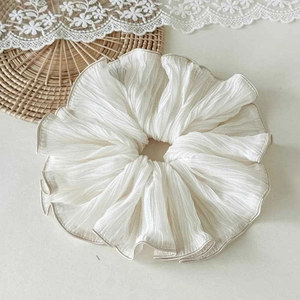 Detailed close-up of large white pleated scrunchie with delicate ruffled edges texture