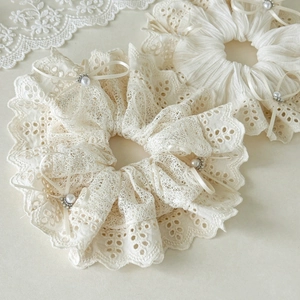Detailed macro view of two cream lace scrunchies with satin bows and pearl beads