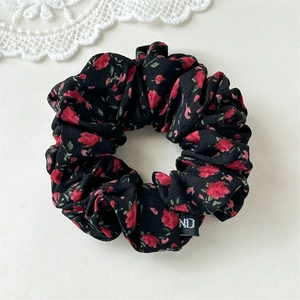 Détail d'un chouchou en tissu noir à fleurs rouges avec une petite étiquette tissée