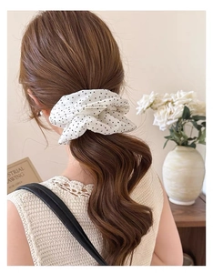 Close-up of a large white scrunchie with black polka dots styled in a low ponytail