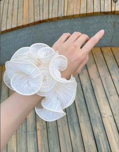 Close-up of a large cream ruffled organza scrunchie with floral petal design on a wrist