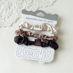 Nahaufnahme des dreiteiligen Satin-Scrunchie-Sets in Champagner und Braun mit Markenetiketten