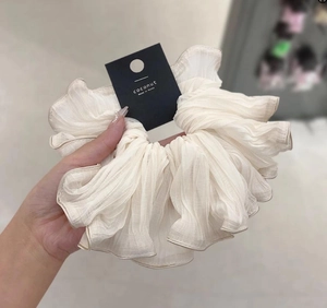 Detail view of a cream pleated scrunchie with fine gold trim and a brand tag