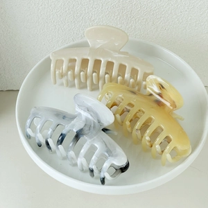 Three elegant hair claws with marble and cream patterns on a ceramic plate