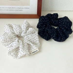Detail of black and white polka dot chiffon hair scrunchies with brand label on table