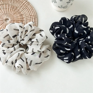 Detailed view of two oversized black and white striped chiffon scrunchies on a cream surface
