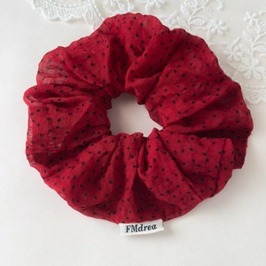 Close-up of red polka dot fabric scrunchie featuring a white branded woven label