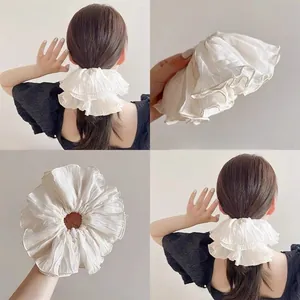 Detailed macro view of off-white pleated chiffon scrunchie with layered wavy edges