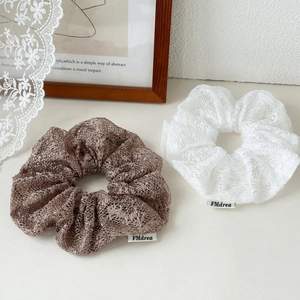 Detailed close-up of lace scrunchies in coffee and white colors with logo tag