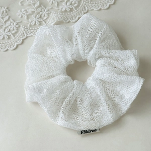 Detailed macro view of white lace scrunchie featuring elegant wave edges and woven logo label