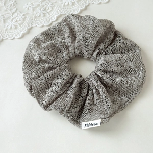 Detailed macro view of a silver-grey mesh scrunchie featuring a white woven brand label