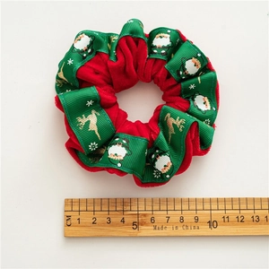 Detail of red velvet Christmas scrunchie with Santa and reindeer patterns next to a ruler