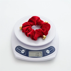 Detail shot of a red velvet Christmas scrunchie with gold bells on a digital scale