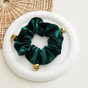 Detailed view of dark green velvet scrunchie with three small gold bells on white tray