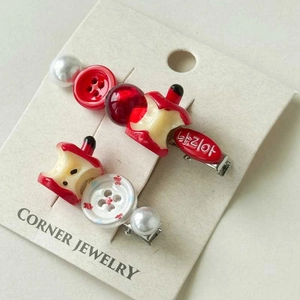 Detailed macro view of two Korean apple-themed hair clips with pearls and resin buttons