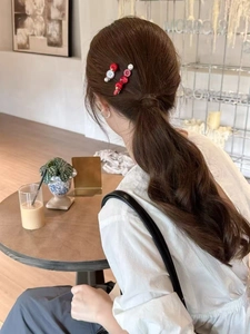 Detail showing two sweet red and white beaded apple hair clips worn by a model in a cafe