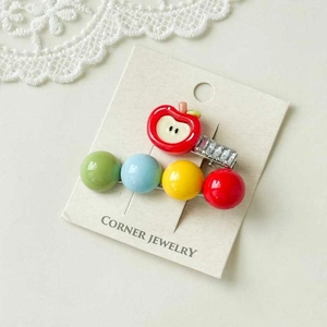 Detail of red apple and colorful beads on metal hair clips set on lace background