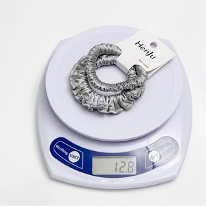 Close-up of two grey satin hair scrunchies on an electronic scale showing 12.8g weight