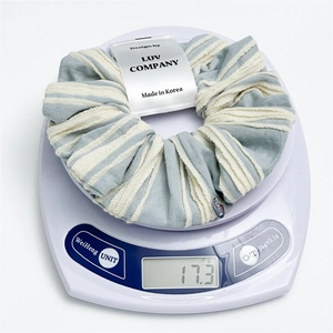 Close-up of striped scrunchie fabric detail with branded label on white scale
