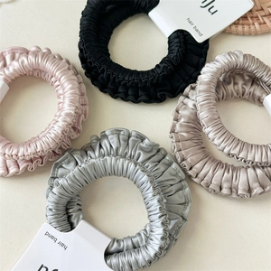 Detail of satin scrunchies in black, pink, grey and beige on brand display cards