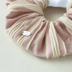 Detailed close-up of pink and beige striped knitted hair scrunchie with silver metal star tag