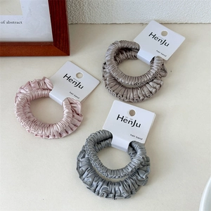 Detailed view of high-elasticity satin scrunchies in pink, khaki, and dark grey set