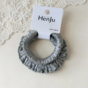 Detail of grey satin hair scrunchie with ruffled edges on branded packaging card