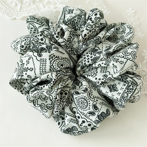 Detail eines weißen Scrunchies mit elegantem schwarzen Paisleymuster und weichen Stofffalten