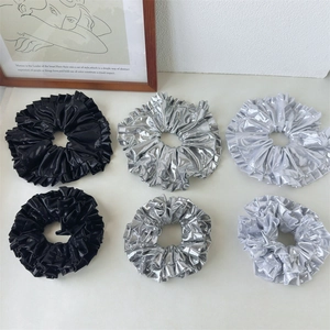 Detailed view of layered metallic scrunchies in silver and black with pleated coating fabric