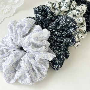 Macro detail of three wide scrunchies with ink wash floral and leaf patterns on fabric