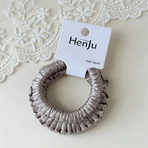 Detailed macro view of champagne gold satin scrunchie with fine pleats on brand card