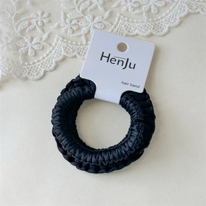Detail view of a black satin scrunchie with pleated texture on a product display card