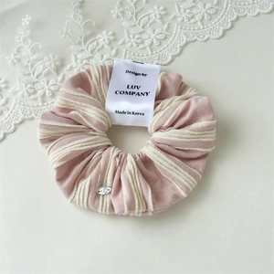Detail of pink and beige striped scrunchie with silver pendant and branded label
