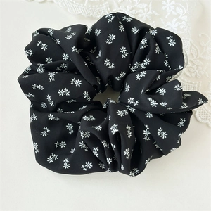 Detail eines Blumen-Scrunchies mit weißen Blüten auf schwarzem weichem Stoff