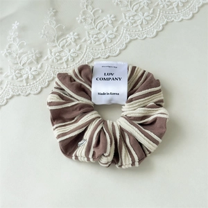 Close-up of striped hair scrunchie with brand label and silver metal charm detail