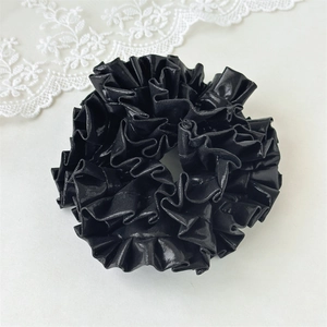 Detailed macro view of black glossy scrunchie with layered fabric pleats and laser sheen