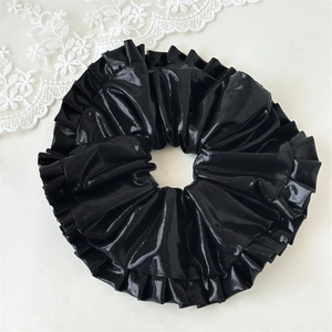Detail of a large black glossy faux leather scrunchie with ruffled texture and lace accent