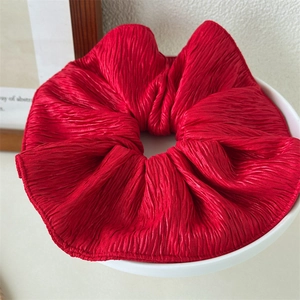 Close-up of a large red pleated scrunchie with glossy texture on a white plate