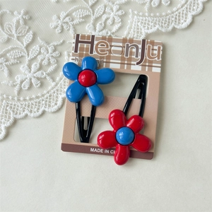 Detail von roten und blauen Blumen-Haarspangen auf Spitze mit Kartonverpackung
