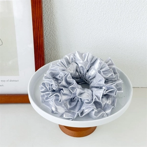 Close-up of a silver laser-reflective fabric scrunchie with pleated texture on a tray