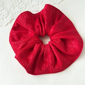 Detail view of red pleated satin scrunchie hair accessory with ruffled fabric texture