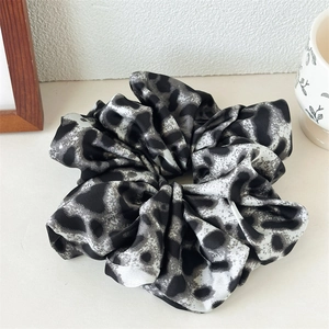 Close-up of leopard print satin scrunchie with soft fabric texture and pleated design
