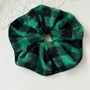 Detailed view of green buffalo plaid scrunchie with sparkling glitter accents and soft texture