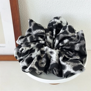 Detail of high-end leopard print scrunchie in black and grey satin fabric on white pedestal