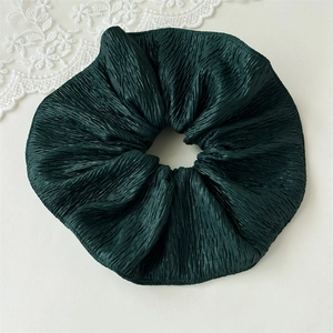 Detail view of a dark green pleated velvet scrunchie with elegant lace background