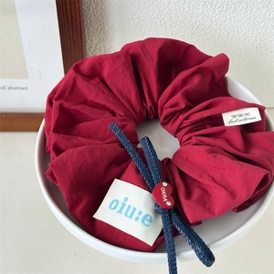 Close-up of a burgundy ruffled hair scrunchie with heart bead and brand labels