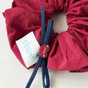 Close-up of red fabric scrunchie with blue denim bow and heart-shaped logo detail