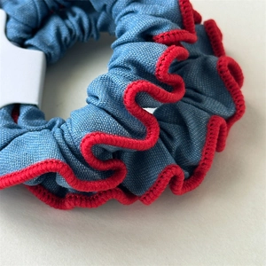 Detailansicht eines Denim-Haargummis mit roten Ziernähten und elastischer Textur