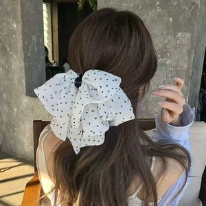 Détail d'une grande pince à cheveux à nœud blanc à pois noirs sur une queue de cheval