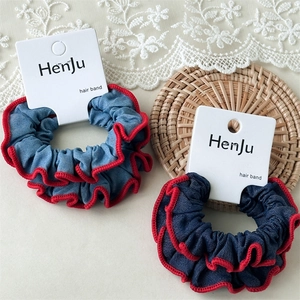Detailaufnahme von zwei Scrunchies im Denim-Stil mit roten Rüschenrändern auf Verpackung